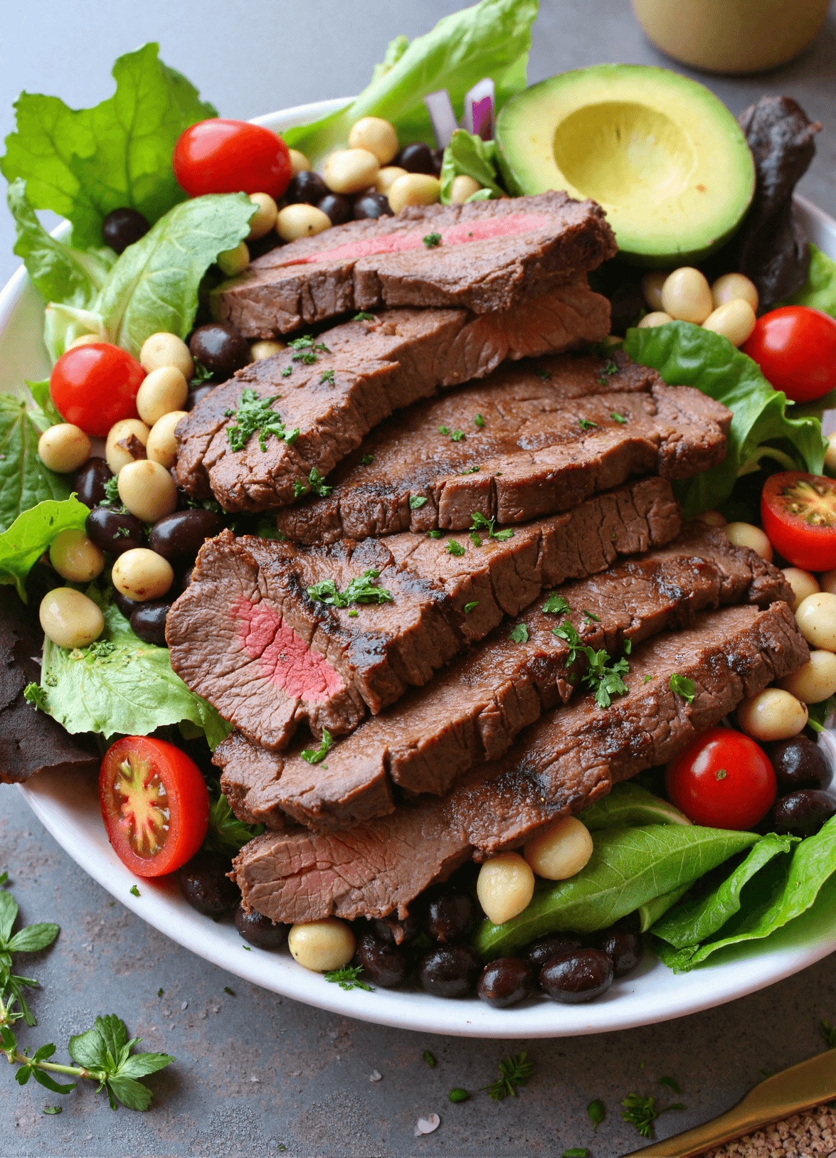 Grilled steak slices served over a vibrant green salad with black beans, cherry tomatoes, avocado slices, and red onion.