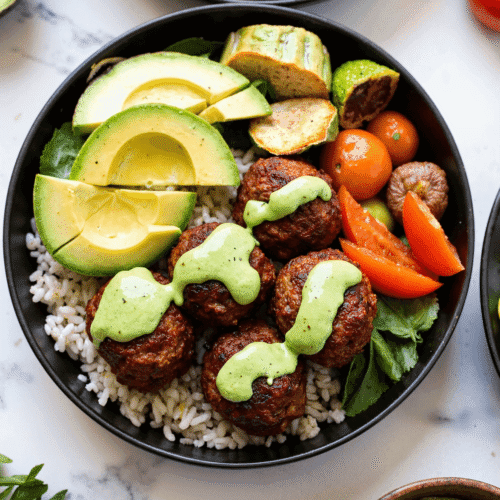 High-protein barbecue meatball bowl with avocado slices, rice, fresh vegetables, and creamy avocado goddess sauce.