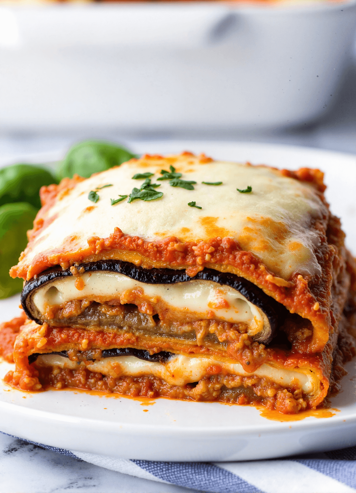 A slice of eggplant lasagna layered with roasted eggplant, melted cheese, rich tomato sauce, and fresh herbs.