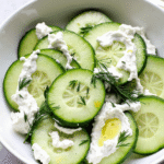 Bowl of cucumber slices with creamy Greek yogurt, fresh dill, and olive oil.
