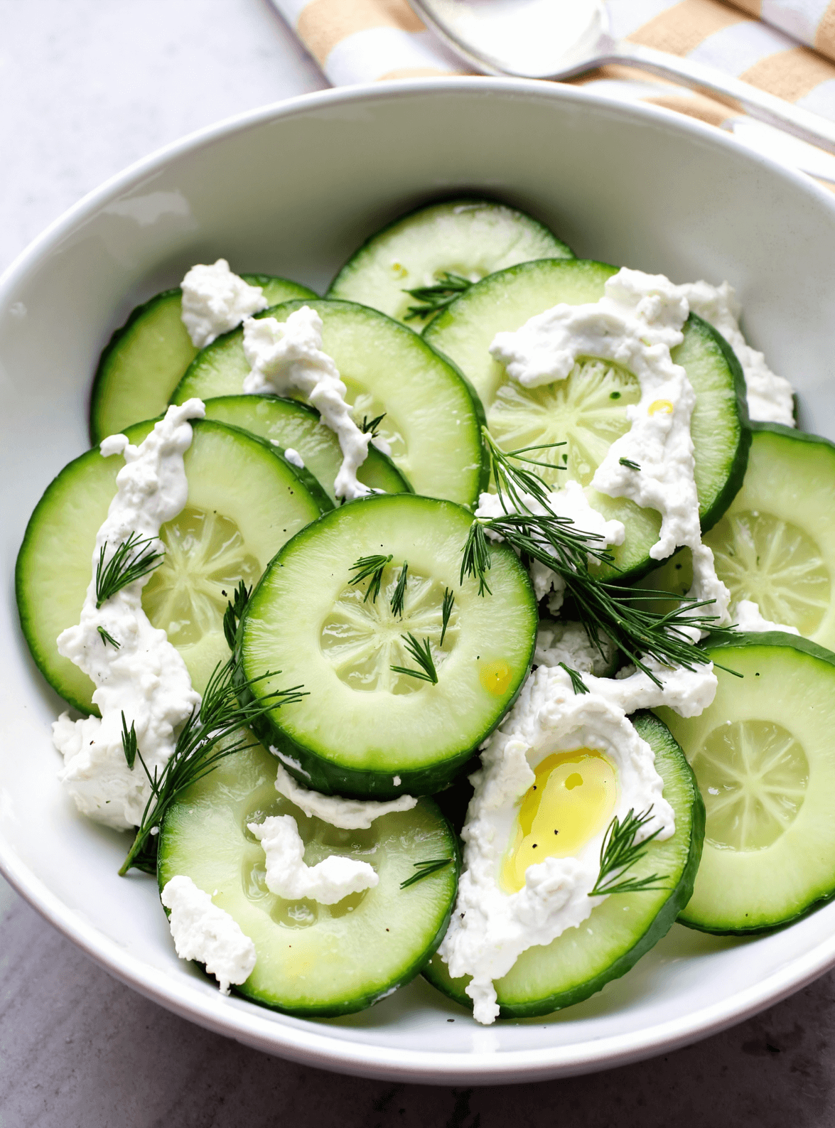 Bowl of cucumber slices with creamy Greek yogurt, fresh dill, and olive oil.