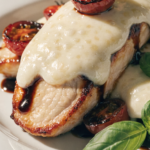 Close-up of balsamic baked chicken breast topped with melted mozzarella, fresh basil, and roasted cherry tomatoes.