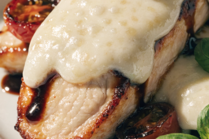 Close-up of balsamic baked chicken breast topped with melted mozzarella, fresh basil, and roasted cherry tomatoes.