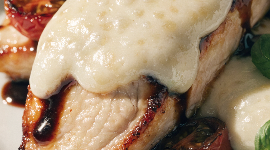 Close-up of balsamic baked chicken breast topped with melted mozzarella, fresh basil, and roasted cherry tomatoes.