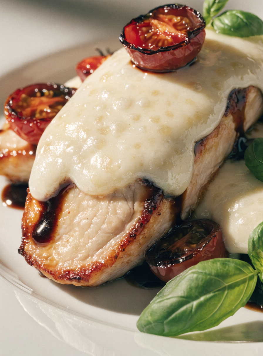 Close-up of balsamic baked chicken breast topped with melted mozzarella, fresh basil, and roasted cherry tomatoes.
