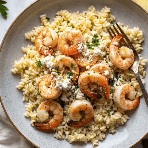 Plated lemon feta orzo shrimp garnished with fresh parsley, served in a rustic ceramic bowl.
