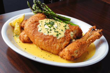 Golden breaded chicken pieces drizzled with garlic butter sauce, garnished with parsley, and served with asparagus and lemon wedges.
