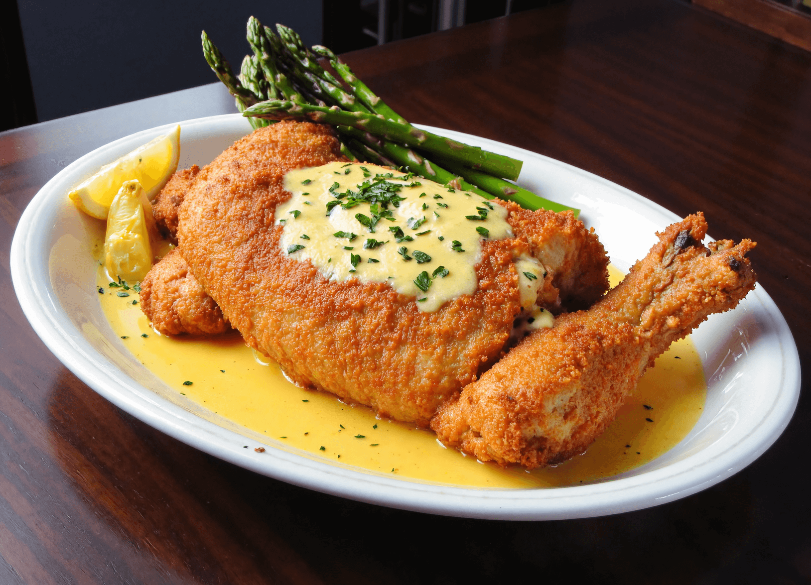 Golden breaded chicken pieces drizzled with garlic butter sauce, garnished with parsley, and served with asparagus and lemon wedges.