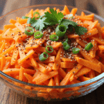 Bowl of spicy carrot salad with sesame seeds, sliced green onions, and fresh cilantro garnish.