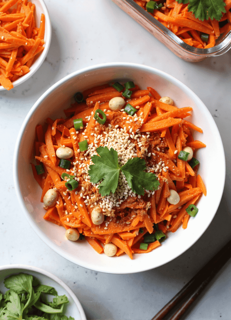 Bowl of spicy viral carrot salad with sesame seeds, cilantro, and peanuts, served with fresh herbs and green onions.