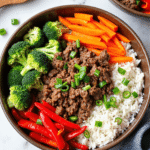 Ground beef rice bowl with broccoli, carrots, red bell peppers, and green onions served in a brown bowl.