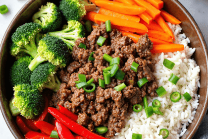 Ground beef rice bowl with broccoli, carrots, red bell peppers, and green onions served in a brown bowl.