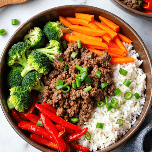 Ground beef rice bowl with broccoli, carrots, red bell peppers, and green onions served in a brown bowl.