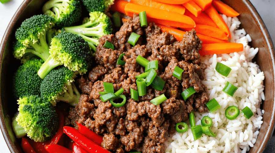 Ground beef rice bowl with broccoli, carrots, red bell peppers, and green onions served in a brown bowl.