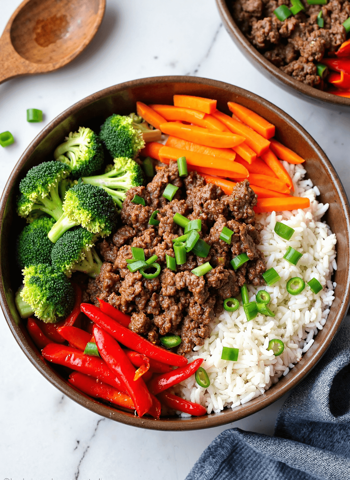 Ground beef rice bowl with broccoli, carrots, red bell peppers, and green onions served in a brown bowl.