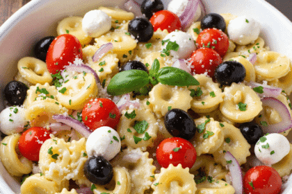 Italian pasta salad made with cheese tortellini, cherry tomatoes, black olives, red onions, and mini mozzarella balls in a white bowl.