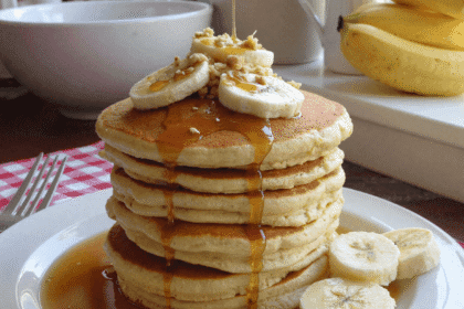 Tall stack of banana cottage cheese pancakes drizzled with maple syrup, topped with banana slices and walnuts, served on a white plate for a high-protein breakfast.