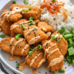 Plate of air-fried bang bang salmon bites drizzled with spicy mayo sauce, served with rice, green onions, and steamed greens.