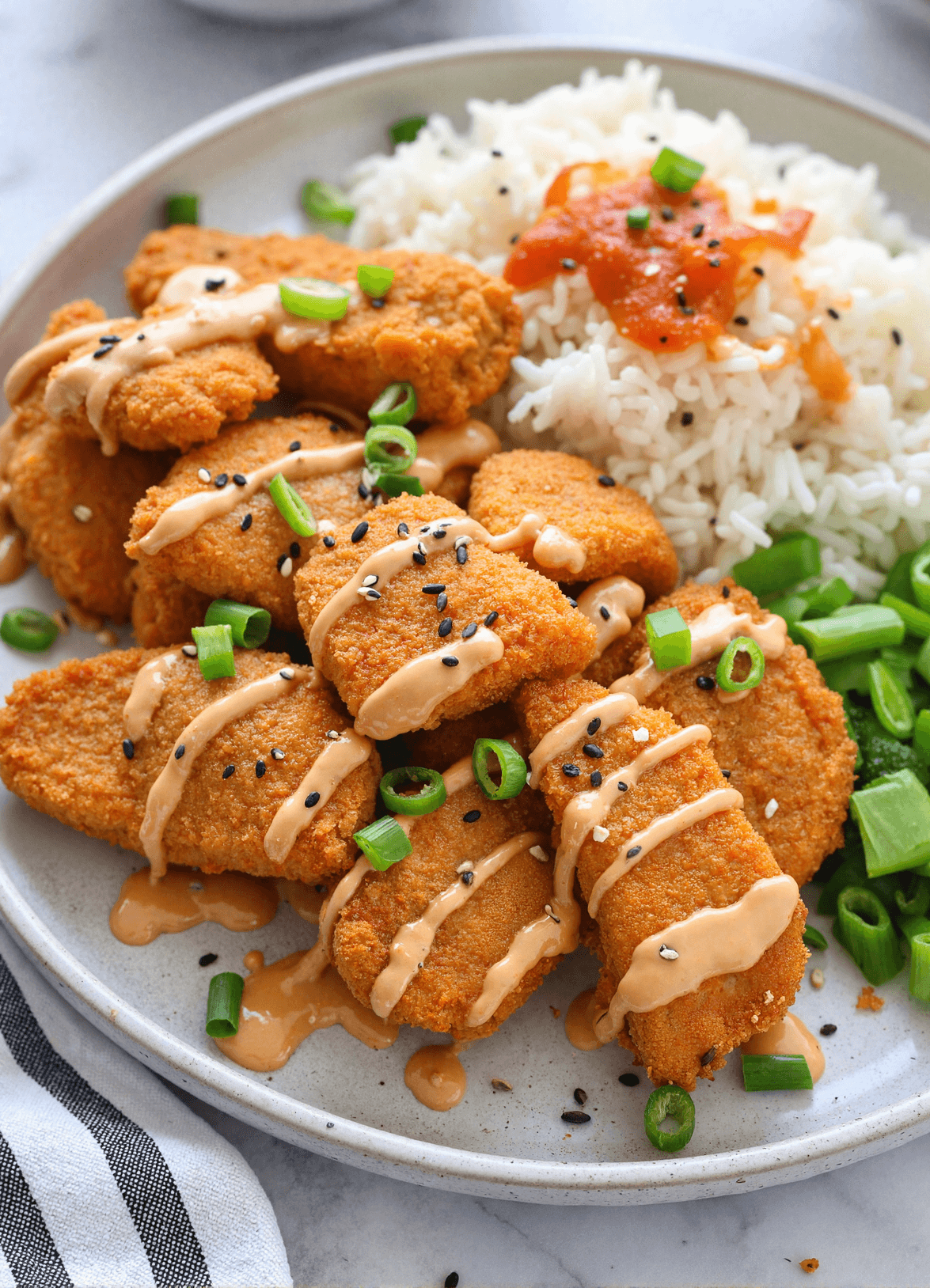 Plate of air-fried bang bang salmon bites drizzled with spicy mayo sauce, served with rice, green onions, and steamed greens.