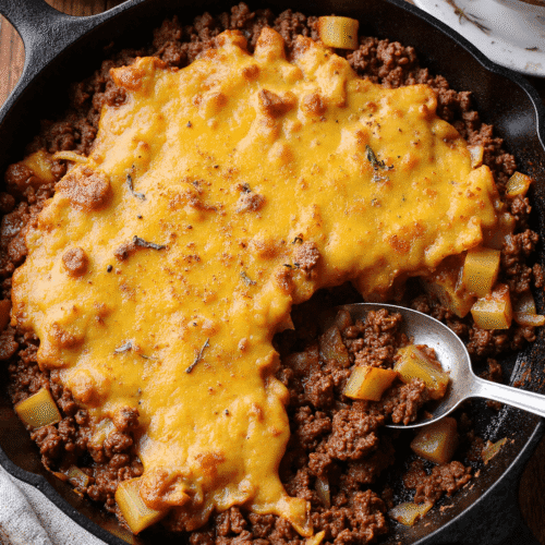 Top view of cheesy ground beef and potato skillet in a cast-iron pan with melted cheese on top.
