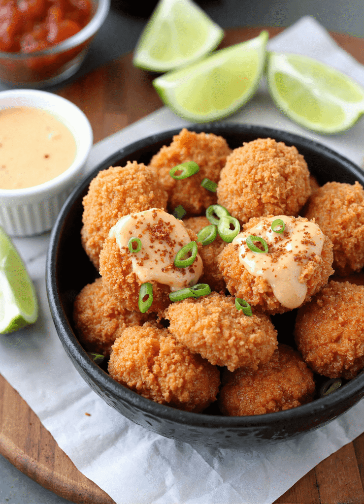 Air-fried crispy bang bang salmon bites topped with spicy creamy sauce and scallions in a black bowl with lime wedges on the side.