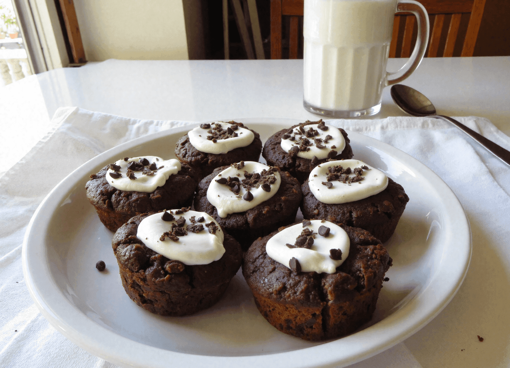 A plate of seven Greek yogurt chocolate oatmeal cups topped with creamy yogurt and mini chocolate chips, served with a glass of milk.