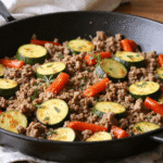 Skillet filled with cooked ground turkey, zucchini slices, and red bell peppers, garnished with fresh herbs.
