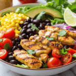 Grilled chicken salad bowl with corn, black beans, avocado, cherry tomatoes, and red onion on a bed of greens.
