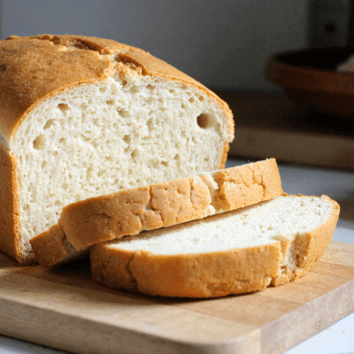 Golden crusted zero carb bread sliced on a wooden cutting board with airy texture and soft interior visible.