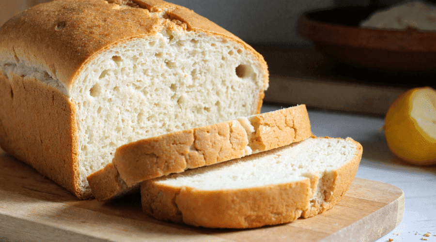 Golden crusted zero carb bread sliced on a wooden cutting board with airy texture and soft interior visible.