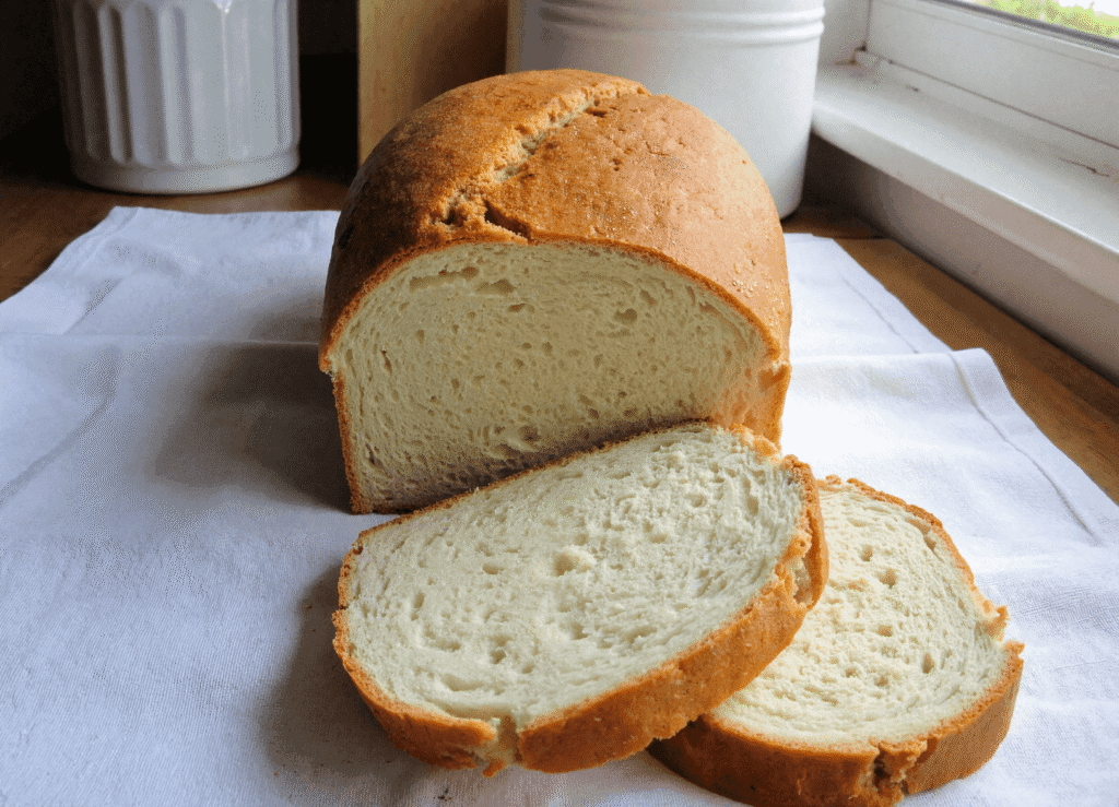 Sliced zero carb yogurt bread showing its fluffy, moist crumb and golden crust on a white cloth beside a sunny window.