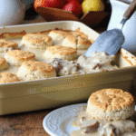 Southern-style biscuits and sausage gravy casserole served fresh in a baking dish with a golden biscuit on a plate.