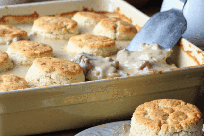 Southern-style biscuits and sausage gravy casserole served fresh in a baking dish with a golden biscuit on a plate.