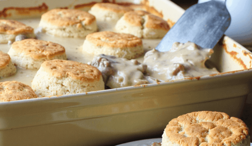 Southern-style biscuits and sausage gravy casserole served fresh in a baking dish with a golden biscuit on a plate.