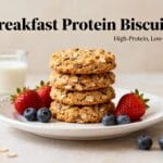 High-protein breakfast biscuits with oats and seeds stacked on a plate with fresh strawberries, blueberries, and a glass of milk.