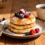 Gluten-free cottage cheese pancakes topped with fresh raspberries, blueberries, powdered sugar, and honey.