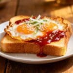 Toast topped with fried eggs drizzled with gochujang sauce, sesame seeds, and scallions.
