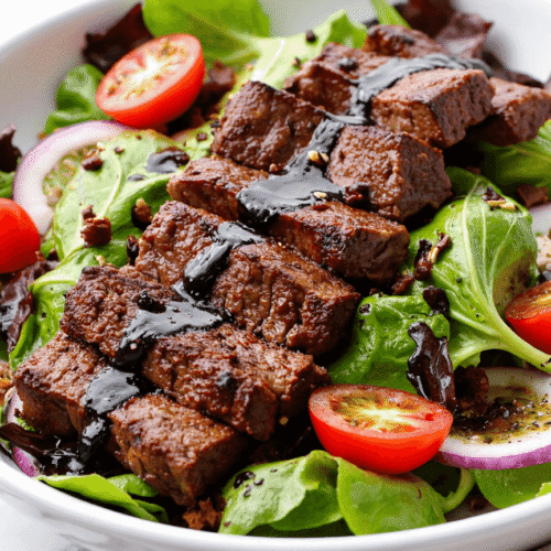 Juicy grilled steak strips drizzled with balsamic glaze over mixed greens, cherry tomatoes, and onions.