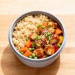 Meal prep container filled with honey garlic chicken fried rice, vegetables, and sesame seed garnish.