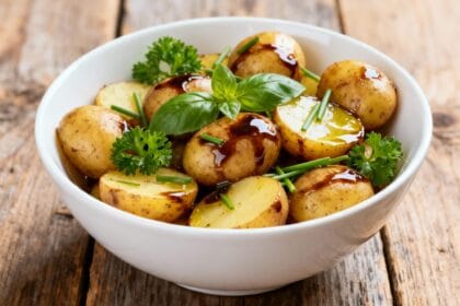 Mayo-free balsamic potato salad with golden potatoes, olive oil drizzle, and basil garnish in a white ceramic bowl.