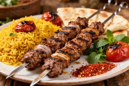 Grilled Persian koobideh beef kebabs with saffron rice, flatbread, fresh mint, and roasted tomatoes.
