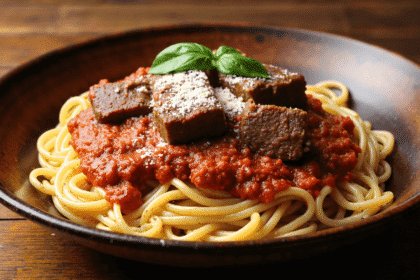 Pasta with braised short rib ragu, tomato sauce, parmesan cheese, and basil served on a dark plate.