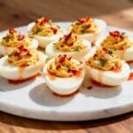 Deviled eggs topped with chili flakes, herbs, and drizzled with spicy Sriracha garlic sauce.