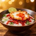 Crispy fried egg served over rice with chili sauce, lime, fresh herbs, and sliced red chili.