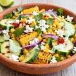Mexican street corn cucumber salad with grilled corn, cucumbers, red onion, cilantro, cotija cheese, and lime crema in a clay bowl.