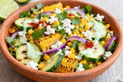 Mexican street corn cucumber salad with grilled corn, cucumbers, red onion, cilantro, cotija cheese, and lime crema in a clay bowl.