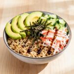 Sushi bowl with brown rice, avocado, cucumber, crab, seaweed, and sesame seeds drizzled with soy glaze.