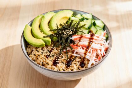 Sushi bowl with brown rice, avocado, cucumber, crab, seaweed, and sesame seeds drizzled with soy glaze.