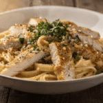 Close-up of creamy garlic Parmesan pasta with sliced chicken served in a bowl, garnished with fresh parsley and black pepper.