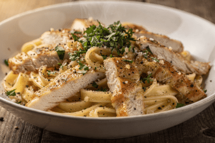 Close-up of creamy garlic Parmesan pasta with sliced chicken served in a bowl, garnished with fresh parsley and black pepper.